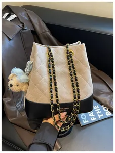 Detailed view of beige quilted bucket bag with chain strap and cute bear charm pendant.
