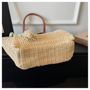 Close-up detail shot of the woven straw tote bag featuring stylish fringe and leather handles.