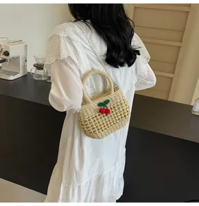 Close-up detail of a pastoral straw woven handbag with cute cherry charm and pearl strap.