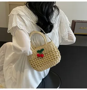 Straw woven bag detail shot featuring a handmade crochet cherry and pearl chain strap.