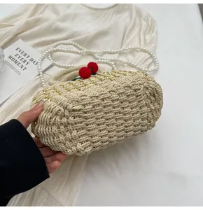Detail shot of straw woven handbag with pearl strap and cute red cherry decoration.
