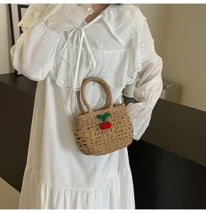 Detail view of pastoral straw woven bag featuring cute cherry decor and pearl chain strap.