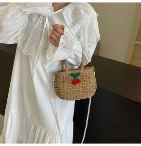 Detail view of pastoral style straw woven handbag featuring pearl strap and cherry decor.
