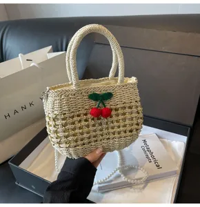 Detail view of a woven straw handbag featuring cute crochet cherry decor and pearl strap.