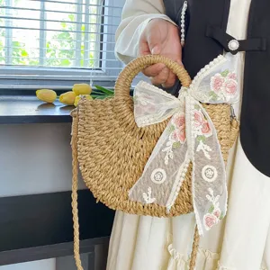 Vista detallada del bolso de hombro de paja estilo pastoral con lazo de encaje floral.