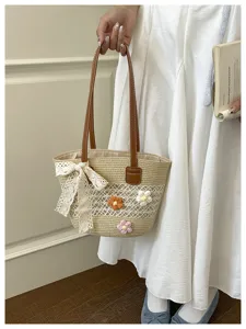 Détail de sac porté épaule en paille tissée avec décorations florales et élégant nœud en dentelle.