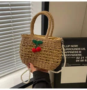 Woven straw handbag detail with cute cherry decor and elegant pearl shoulder strap.