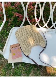 Scène extérieure d'un sac à bandoulière en paille tissée chic avec lanière en cuir et livre.
