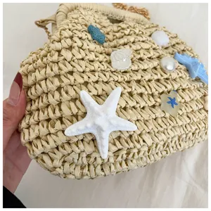 Dettaglio in primo piano della borsa in paglia da spiaggia con ciondoli a stella di mare.