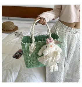 Chic green woven straw tote bag with cute plush rabbit pendant and stylish ribbon handle.