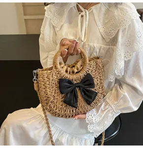 Primer plano del bolso de paja tejido con un lazo negro elegante y asas superiores resistentes.