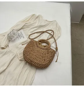 Detalle de un bolso de mano de paja tejida con asa redonda y correa en tela blanca.