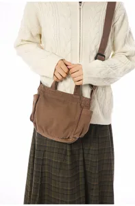 Detailed view of a brown canvas crossbody shoulder bag with side pockets, held by a model.