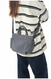 Detail shot of grey canvas crossbody bag worn on shoulder, showing side pocket and strap design.