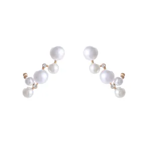 Detailopname van asymmetrische oorbellen met glanzende witte parels en schitterende steentjes.