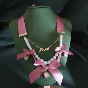 Detailed close-up of the vintage pink ribbon bow pearl necklace with metal Love pendant.