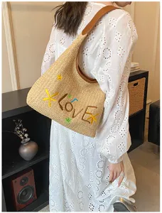 Dettaglio borsa a spalla in paglia intrecciata, lettere LOVE ricamate, stile vacanza estiva.