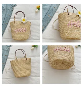 Straw woven bag detail shot showing the pink embroidered lettering and natural texture.