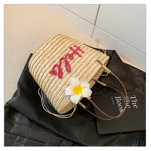 Straw woven bucket handbag with cute pink letter embroidery and flower decor for summer beach.