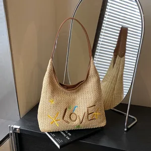 Primo piano di una chic borsa a spalla in paglia con ricamo Love e cinturini marroni.