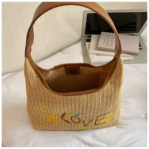 Dettaglio in primo piano della borsa in paglia estiva con manico in ecopelle e ricamo LOVE.