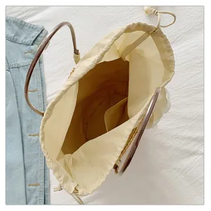 Detail view of straw woven bag interior, beige fabric drawstring lining and metal handles.