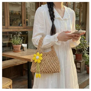 Detail shot of a hollow woven net handbag with yellow flower pendant in a cafe scene.
