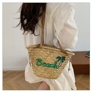 Vue détaillée d'un sac de plage en paille tissée avec broderie Beach et patch de palmier.