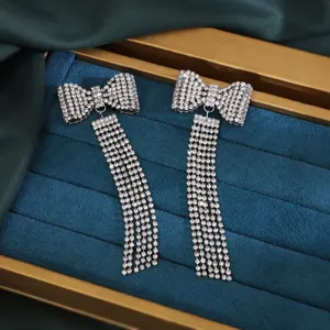 Close-up detail of sparkling rhinestone bow tassel earrings on blue velvet tray.