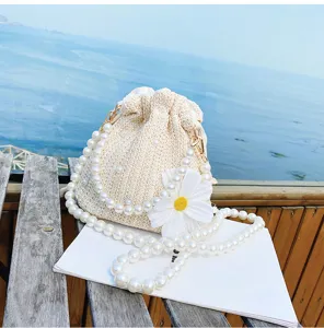 Close-up of elegant pearl chain strap and white daisy flower detail on woven resort bucket bag.