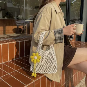 Detailed view of a white knitted net bag with a cute yellow flower charm in a cafe.