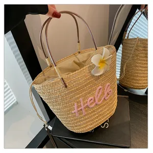 Sweet woven straw bucket bag with floral decor and pink letter embroidery for beach vacation.