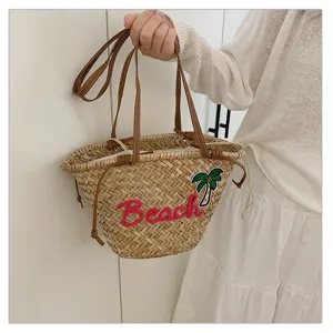 Vue détaillée du sac de plage en paille tissée avec broderie Beach et poignées en cuir.