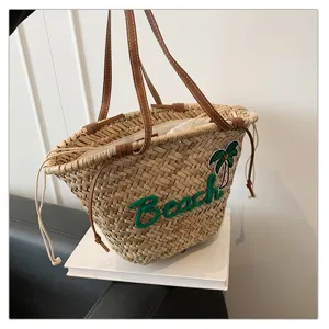 Vue detaillee du sac de plage en paille avec broderie verte et motif de cocotier estival.