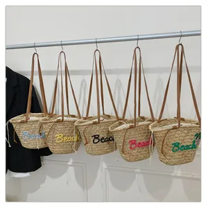 Vue rapprochée de sacs de plage en paille tressée avec broderie Beach colorée et bretelles.