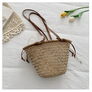 Vue détail d'un sac seau en paille tressée avec des bretelles en cuir marron et cordon.