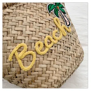 Gros plan détail du sac de plage en paille avec broderie corde Beach jaune et patch palmier.