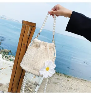 Straw bucket bag with pearl chain handle and white floral detail, perfect resort beach style.