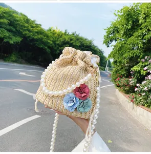 Detail shot of straw bucket bag with pearl chain strap and colorful fabric flowers for beach.
