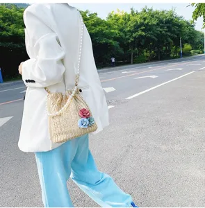 Chic straw woven bucket bag with pearl chain strap and floral decor for summer vacation.