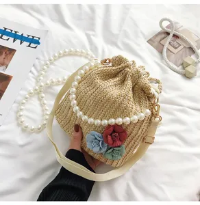 Straw woven bucket bag with pearl chain handle and fabric flowers for summer beach resort.