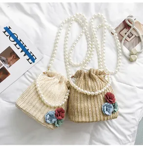 Detail view of woven straw bucket bag featuring pearl chain strap and colorful floral design.