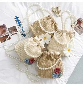 Straw bucket bag with pearl chain handle and floral decor, perfect for summer beach vacation.