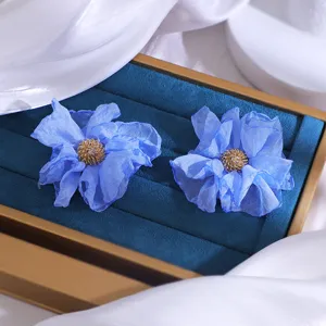 Close-up of handmade blue chiffon flower earrings with golden stamen on a velvet jewelry tray.