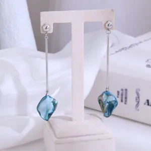 Detailweergave van lange minimalisten oorbellen met metalen staaf en blauwe hanger.