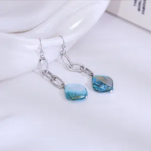 Close-up van lange kettingoorbellen met blauwe natuurlijke schelp-hangers en metaal.