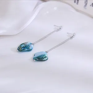 Detailopname van lange oorbellen met onregelmatige blauwe schelphangers en zilveren staafjes.
