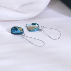 Gedetailleerd overzicht van onregelmatige blauwe schelp oorbellen op een witte stoffen achtergrond.