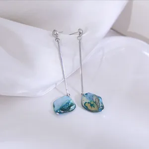 Close-up detailopname van lange zilverkleurige metalen oorbellen met blauwe schelp hangend.