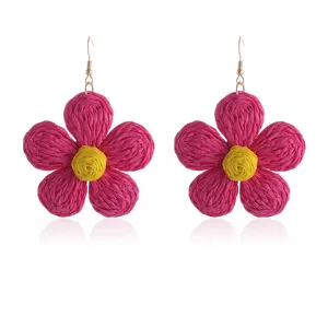Detailopname van gevlochten raffia bloem oorbellen met mooie roze bloemblaadjes.